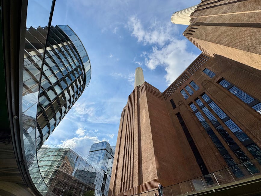 A low-angle view of Battersea Power Station, featuring a mix of modern glass skyscrapers and the historic brick power station structure. The photo captures the sleek, reflective surfaces of the surrounding buildings, the textured brickwork of the power station, and a partly cloudy sky overhead. Visible are glass facades, steel accents, and a concrete column, all contributing to a contemporary cityscape scene. The area appears clean and well-maintained, reflecting the professional surface cleaning services offered by Cleaners SW8, based on this visual evidence of attention to hygiene and upkeep in residential or commercial settings near the Battersea Power Station in SW8.